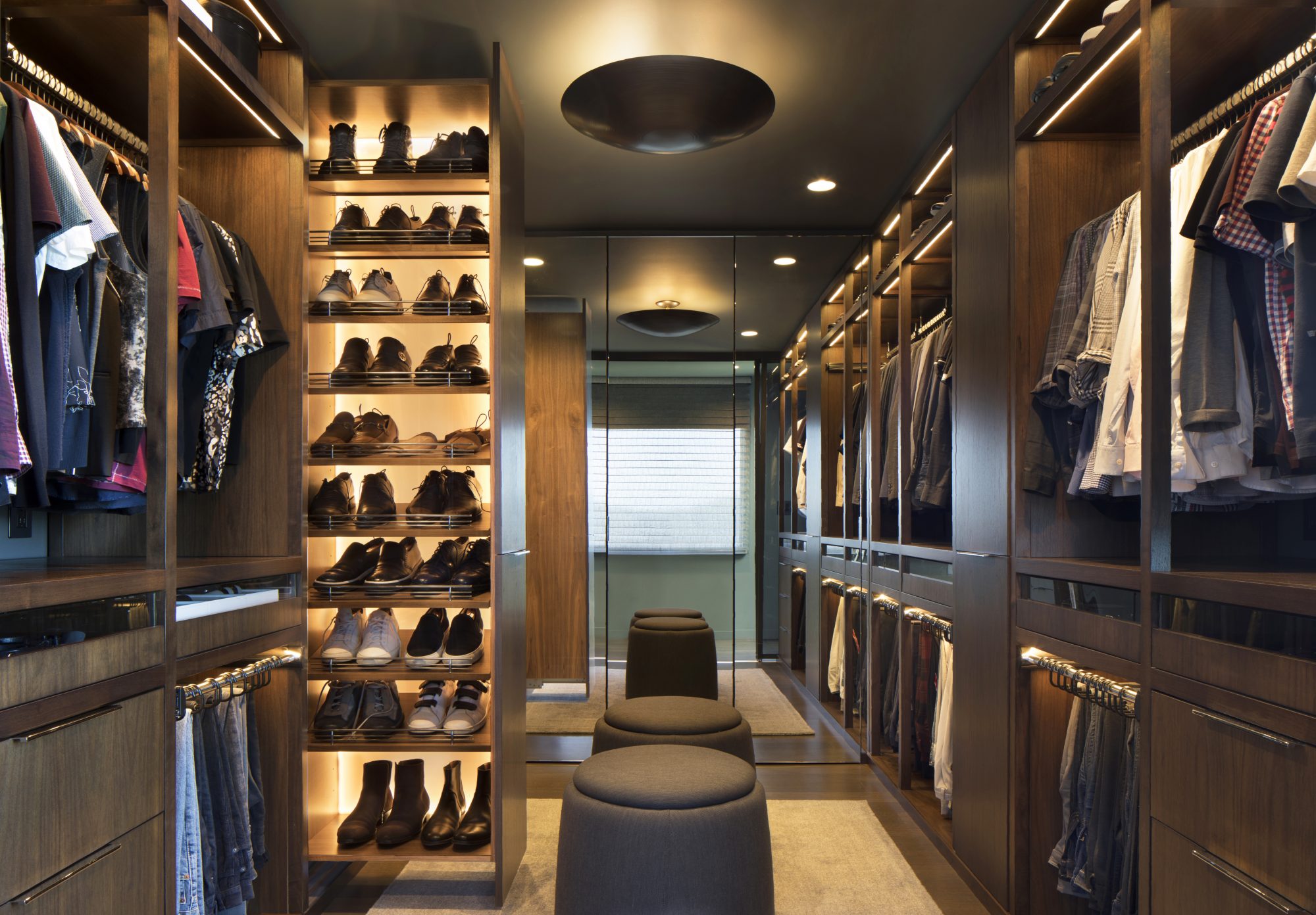 Biltmore walk-in closet with warm wood cabinetry and lit shoe shelving