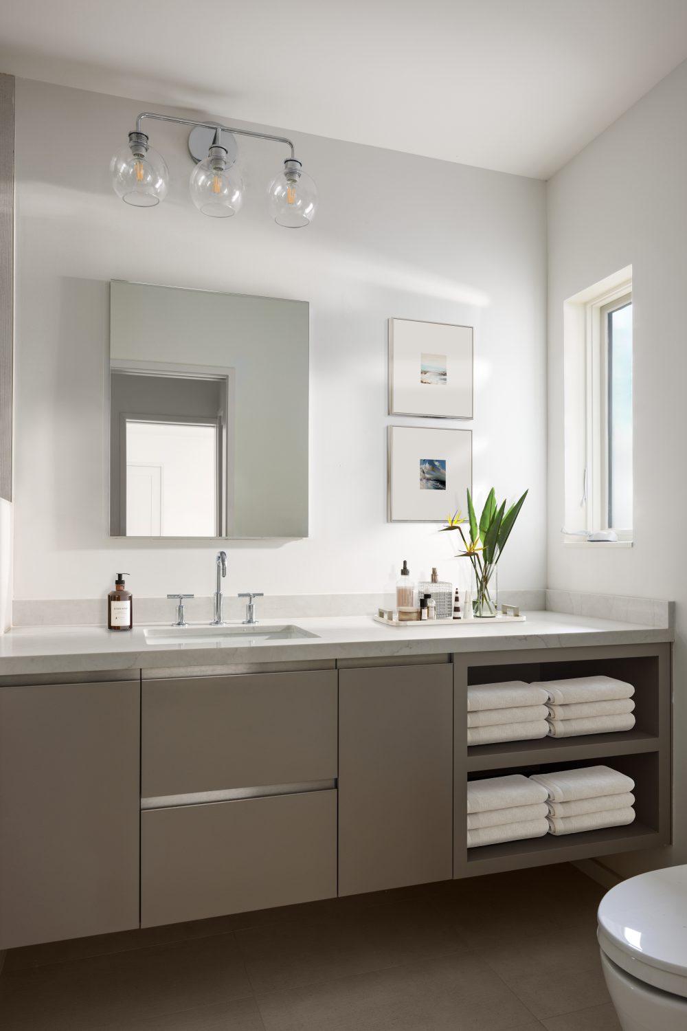 Bathroom vanity with taupe floating cabinets, chrome globe sconces, and coastal art